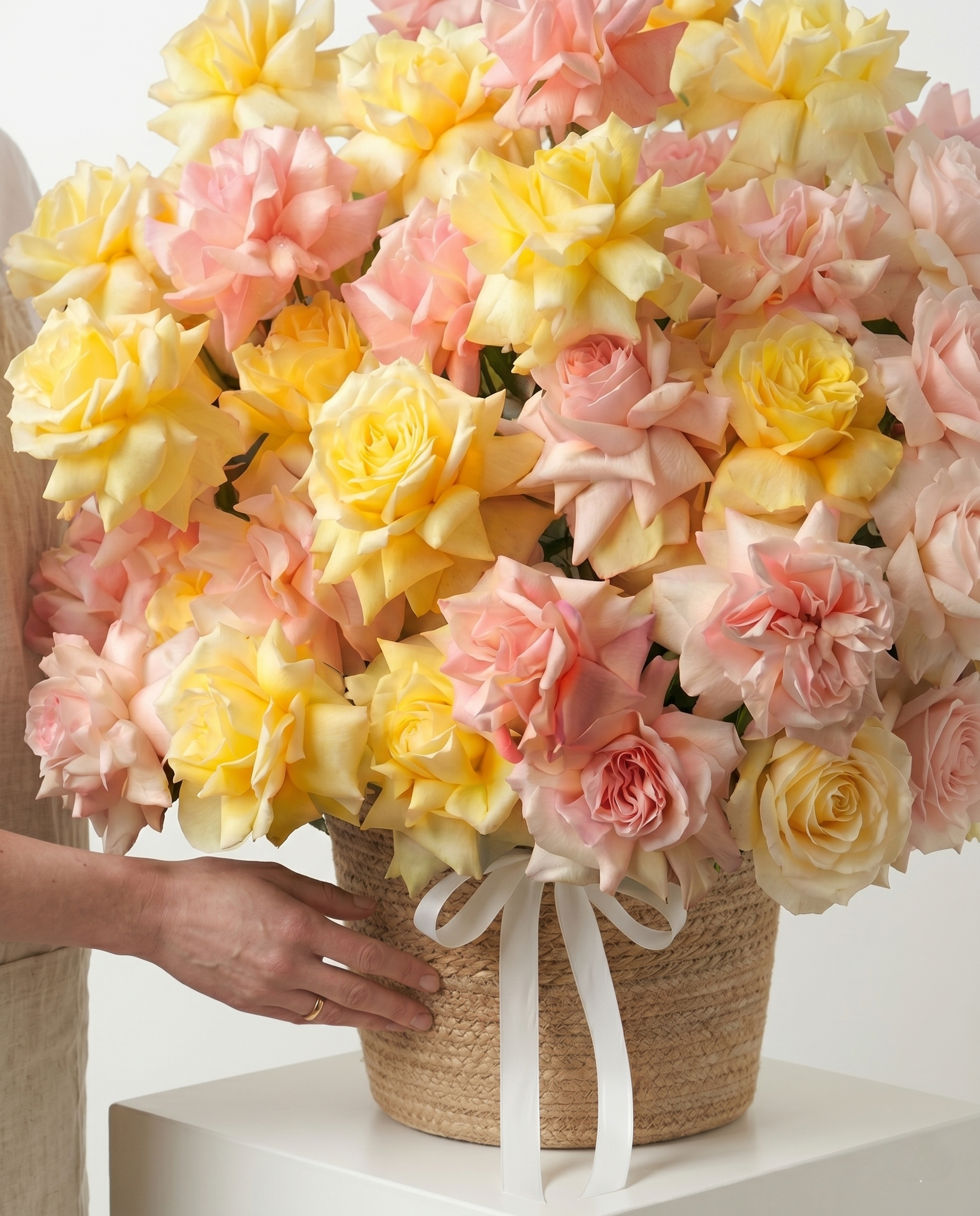 Bouquet of pink and yellow flowers in a woven basket held by a person.
