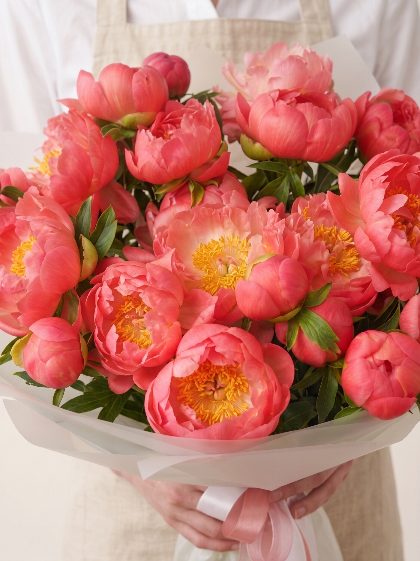 Bouquet of pink peonies with yellow centers held by a person.