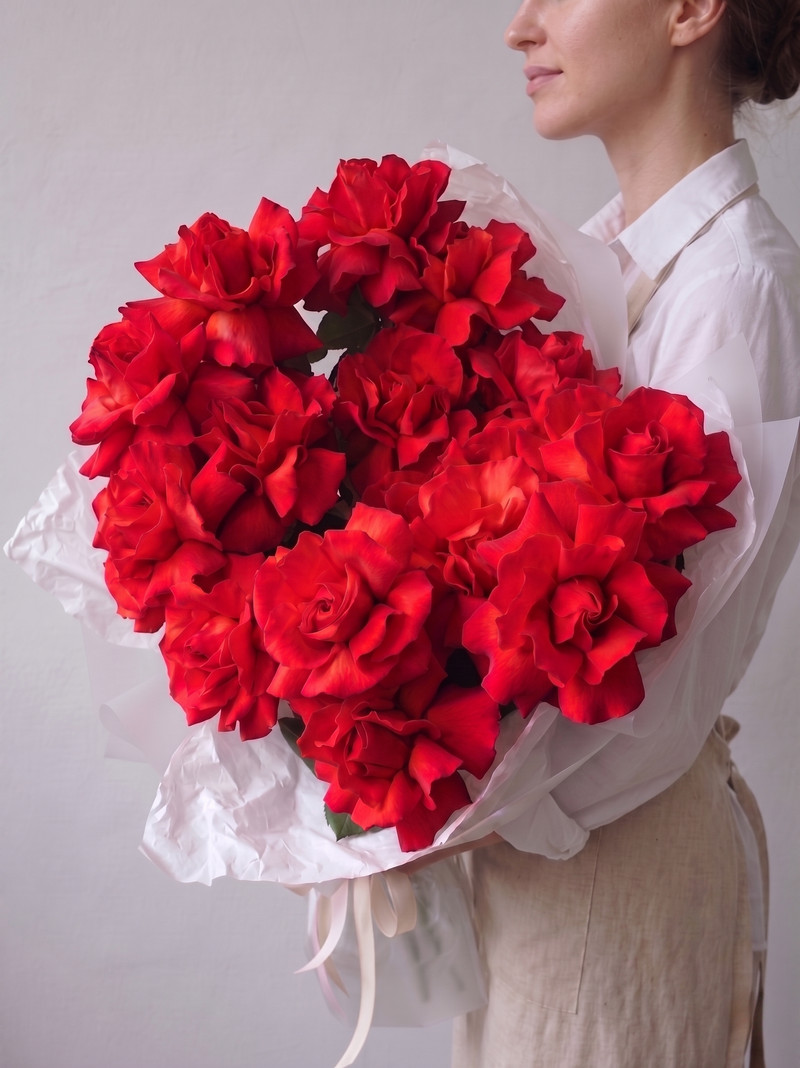 Florist holding a large bouquet of premium red French roses wrapped in white tissue paper — same-day delivery available in Miami, FL