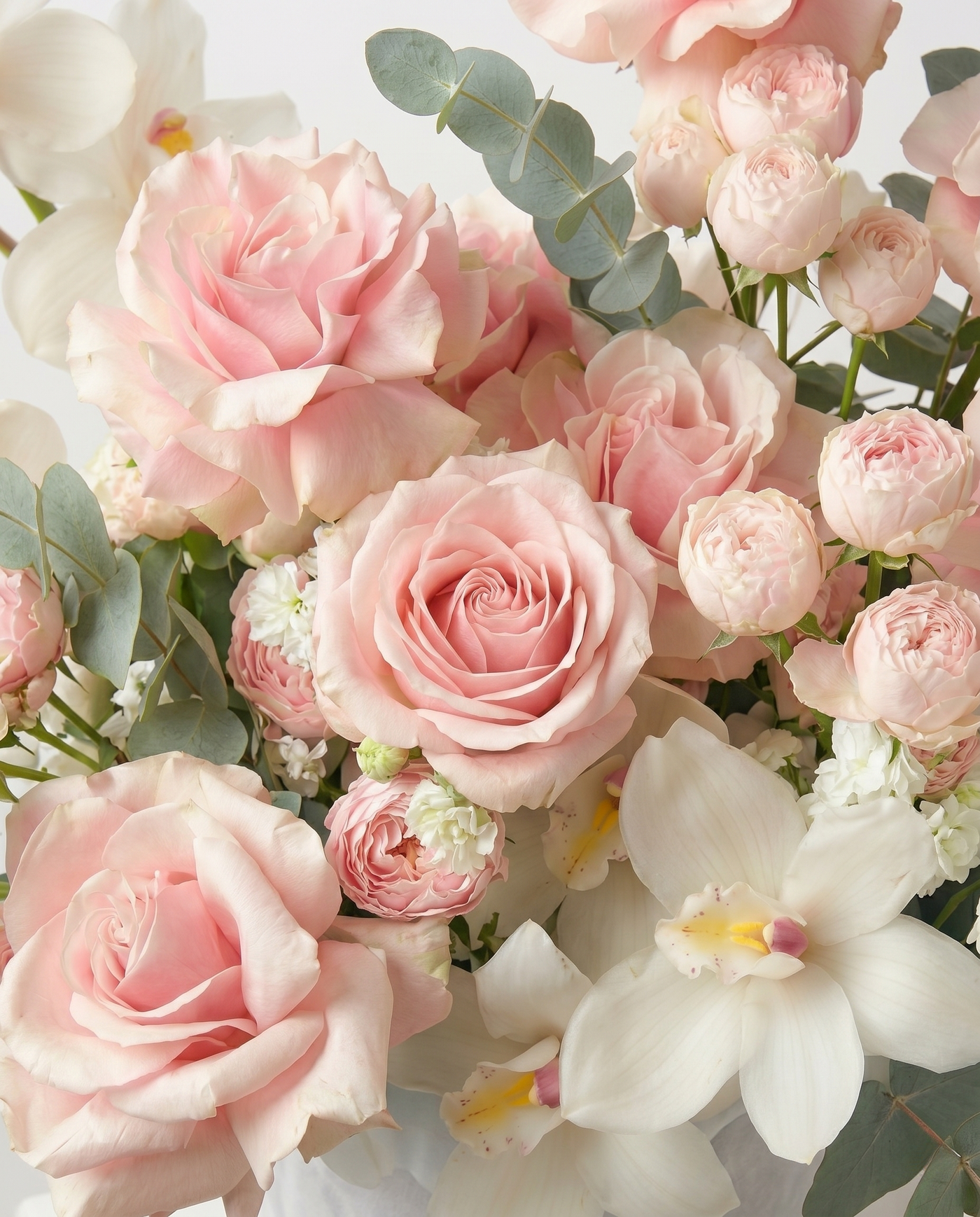 Bouquet of pink roses and white orchids with green leaves.